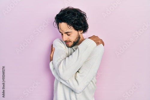 Handsome hispanic man wearing casual white sweater hugging oneself happy and positive, smiling confident. self love and self care © Krakenimages.com