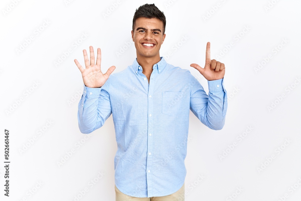 Young hispanic man wearing business shirt standing over isolated background showing and pointing up with fingers number seven while smiling confident and happy. Young hispanic man wearing business shirt standing over isolated background showing and pointing up with fingers number seven while smiling confident and happy.