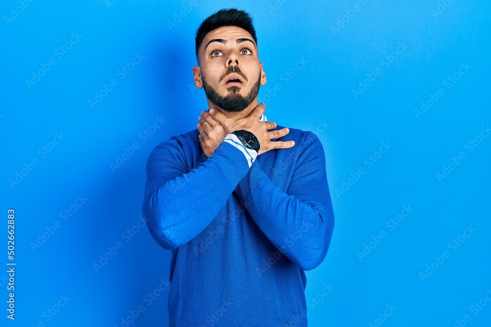 Young hispanic man with beard wearing casual blue sweater shouting suffocate because painful strangle. health problem. asphyxiate and suicide concept. Young hispanic man with beard wearing casual blue sweater shouting suffocate because painful strangle. health problem. asphyxiate and suicide concept.