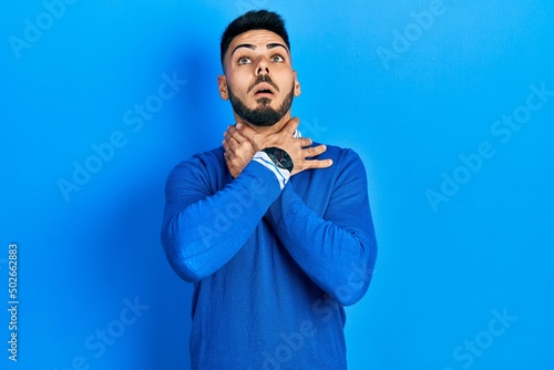 Young hispanic man with beard wearing casual blue sweater shouting suffocate because painful strangle. health problem. asphyxiate and suicide concept.