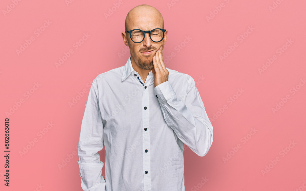 Bald man with beard wearing business shirt and glasses touching mouth with hand with painful expression because of toothache or dental illness on teeth. dentist