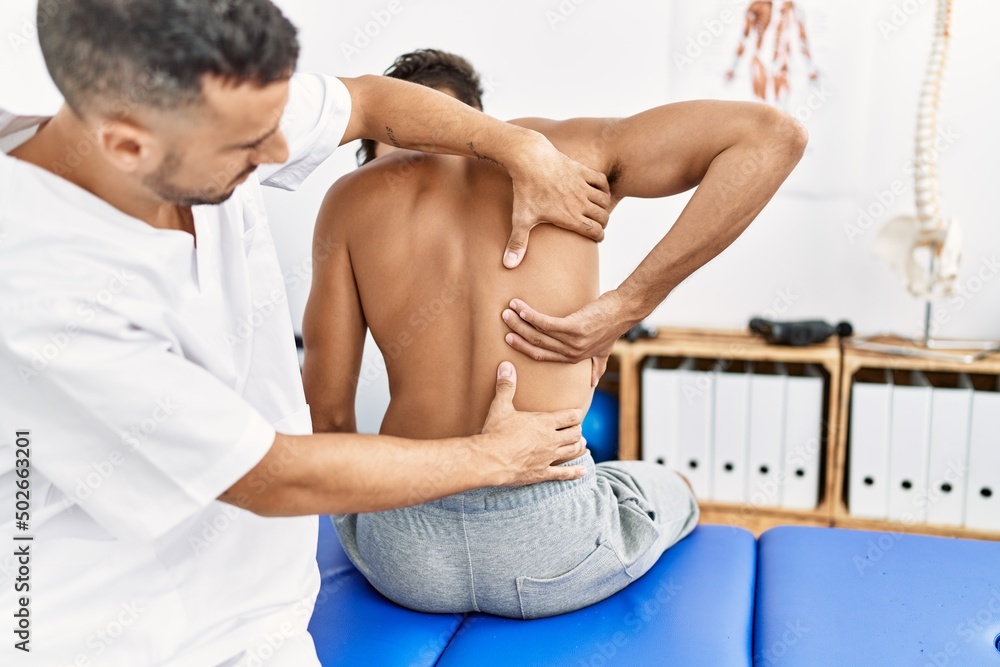 Obraz premium Two hispanic men physiotherapist and patient having rehab session massaging back at clinic