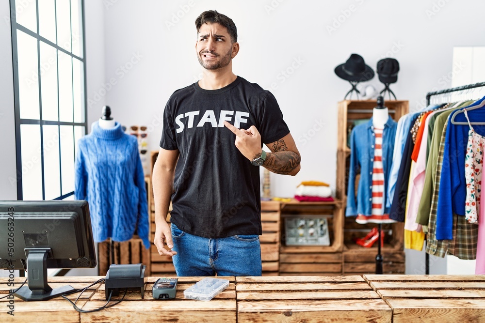 Young hispanic man working at retail boutique pointing aside worried and nervous with forefinger, concerned and surprised expression