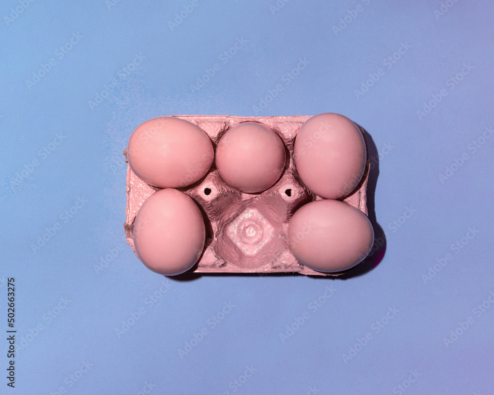 Pastel pink eggs in carton on light blue background. Minimalistic Easter concept. Creative holiday idea. Trendy food inspiration.