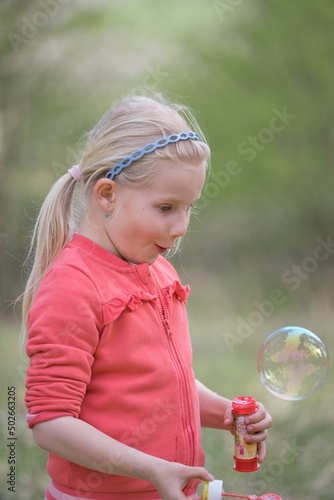 Young happy girl playing in nature with bubble blower