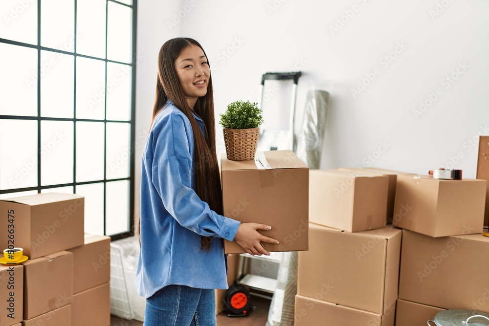 Young chinese girl smiling happy holding cardboard box at new home Young chinese girl smiling happy holding cardboard box at new home
