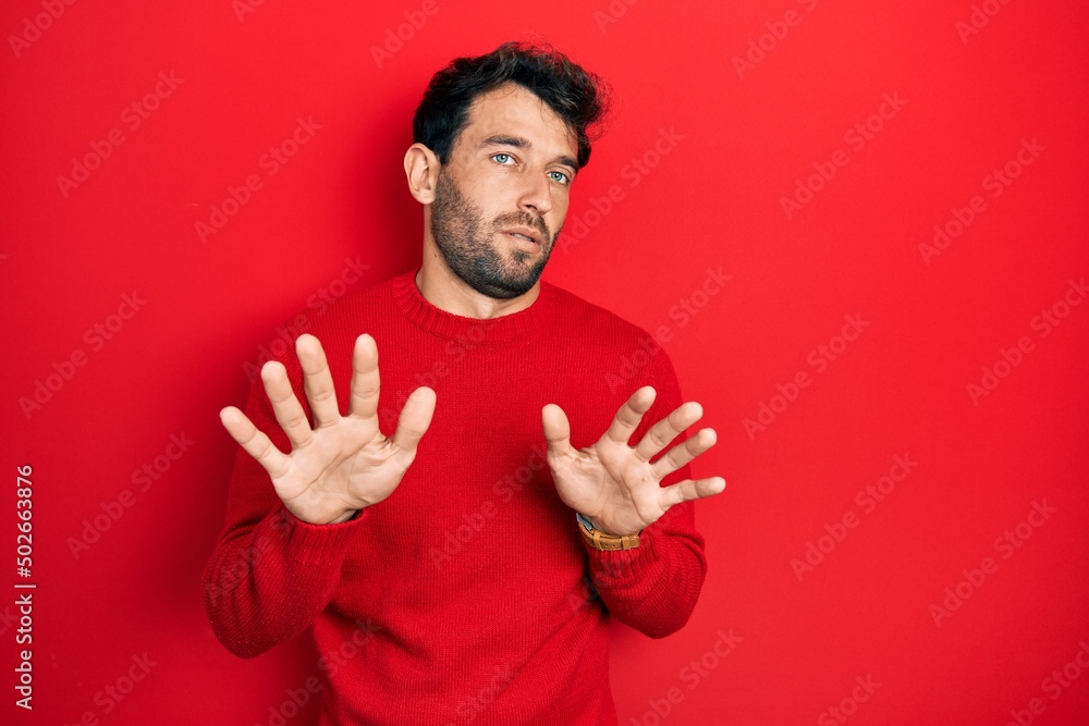 Fototapeta premium Handsome man with beard wearing casual red sweater moving away hands palms showing refusal and denial with afraid and disgusting expression. stop and forbidden.