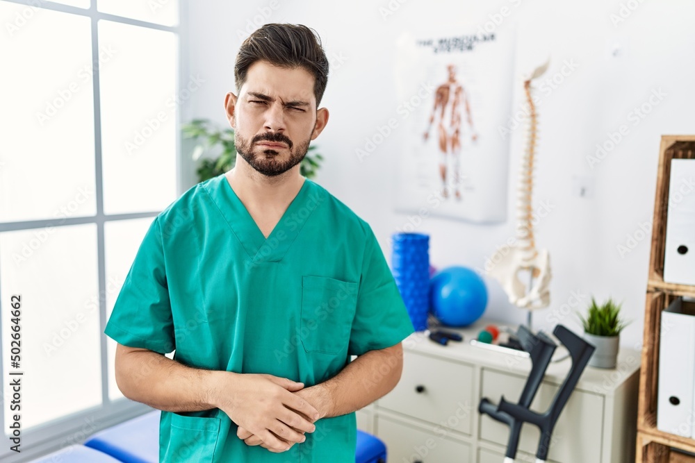 Young man with beard working at pain recovery clinic skeptic and nervous, frowning upset because of problem. negative person. Young man with beard working at pain recovery clinic skeptic and nervous, frowning upset because of problem. negative person.