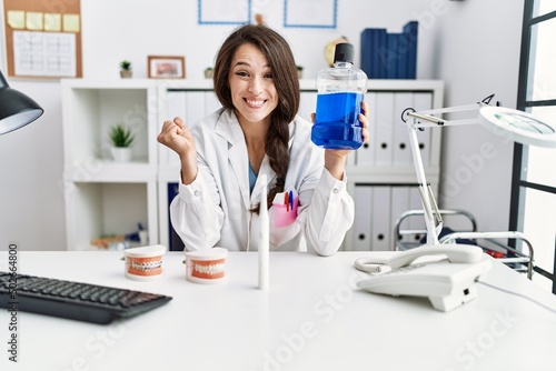 Young dentist woman holding mouthwash for fresh breath screaming proud  celebrating victory and success very excited with raised arm