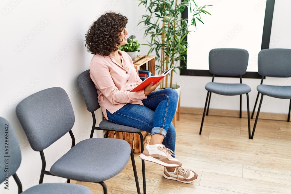 Young middle east woman reading book sitting on chair at waiting room