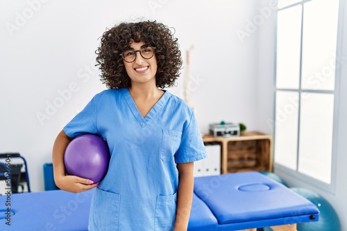 Fototapeta Naklejka Na Ścianę i Meble -  Young middle east woman wearing physio therapist uniform holding fit ball at clinic