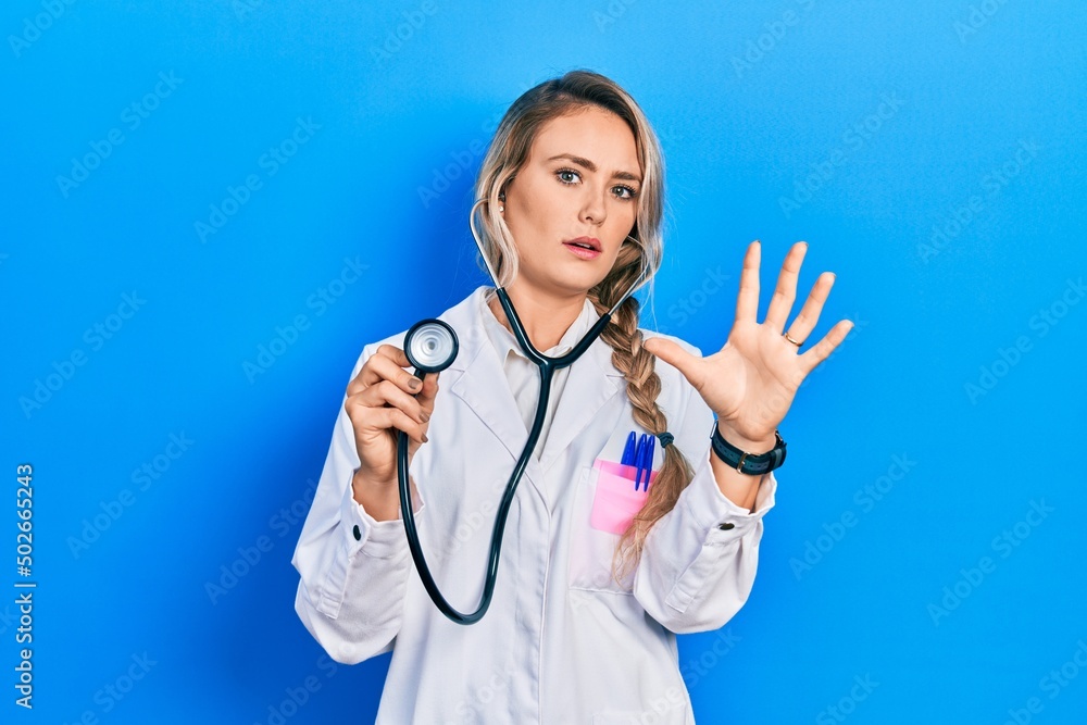 Beautiful young blonde doctor woman holding stethoscope doing stop gesture with hands palms, angry and frustration expression Beautiful young blonde doctor woman holding stethoscope doing stop gesture with hands palms, angry and frustration expression
