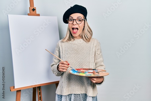 Beautiful caucasian woman drawing with palette on easel stand celebrating crazy and amazed for success with open eyes screaming excited.