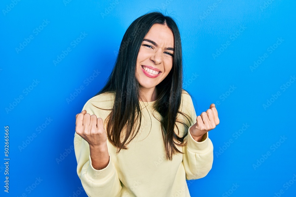 Fototapeta premium Young brunette woman wearing casual sweatshirt very happy and excited doing winner gesture with arms raised, smiling and screaming for success. celebration concept.