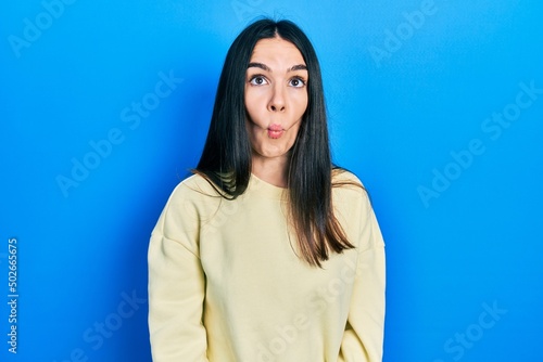 Young brunette woman wearing casual sweatshirt making fish face with lips, crazy and comical gesture. funny expression.