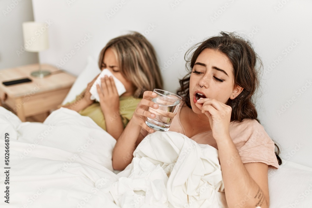 Young ill couple using napkin and eating pills lying on the bed at home.