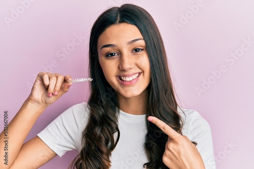 Young hispanic woman holding invisible aligner orthodontic smiling happy pointing with hand and finger