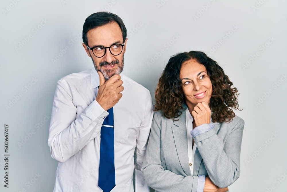 Middle age couple of hispanic woman and man wearing business office uniform with hand on chin thinking about question, pensive expression. smiling with thoughtful face. doubt concept. Middle age couple of hispanic woman and man wearing business office uniform with hand on chin thinking about question, pensive expression. smiling with thoughtful face. doubt concept.