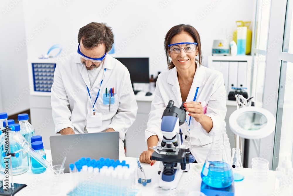 Middle age man and woman partners wearing scientist uniform using laptop and microscope at laboratory Middle age man and woman partners wearing scientist uniform using laptop and microscope at laboratory