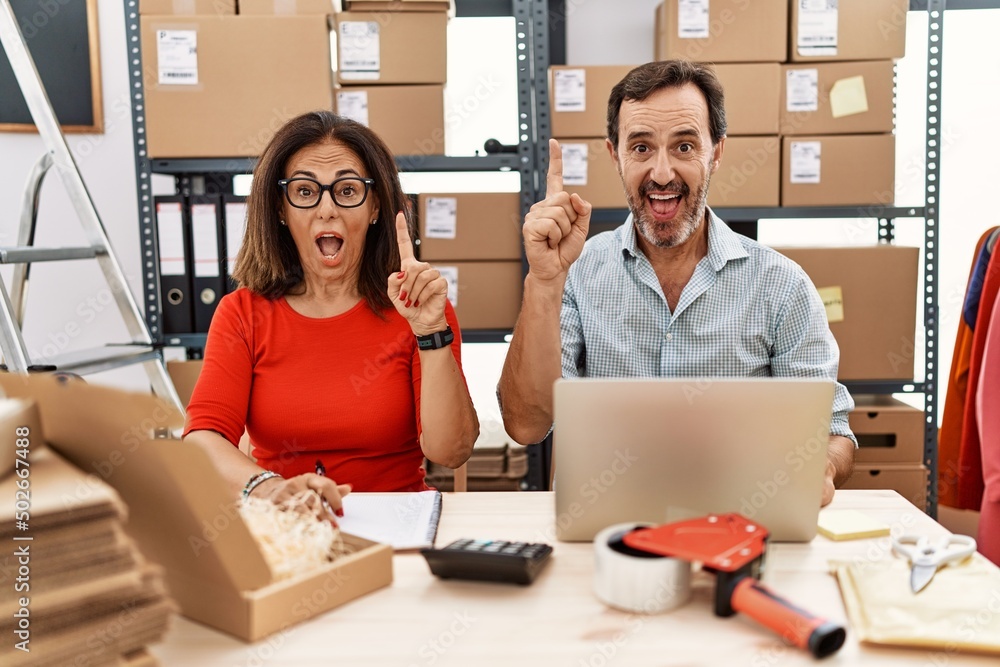Middle age couple working at small business ecommerce pointing finger up with successful idea. exited and happy. number one. Middle age couple working at small business ecommerce pointing finger up with successful idea. exited and happy. number one.