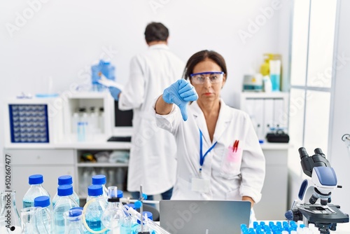 Middle age woman working at scientist laboratory with angry face  negative sign showing dislike with thumbs down  rejection concept