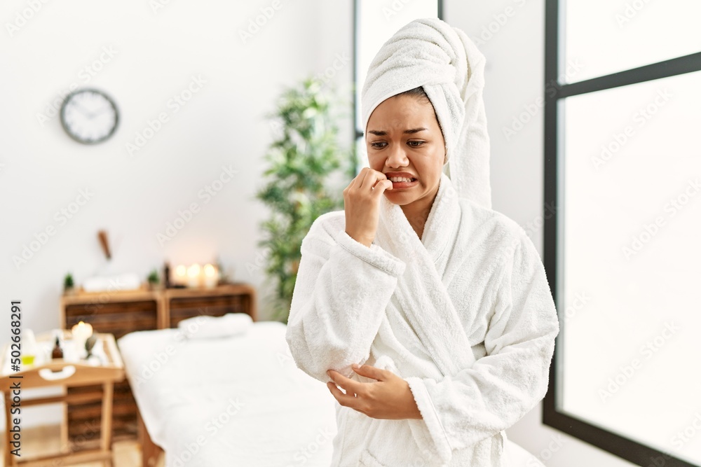 Young brunette woman wearing towel and bathrobe standing at beauty center looking stressed and nervous with hands on mouth biting nails. anxiety problem. Young brunette woman wearing towel and bathrobe standing at beauty center looking stressed and nervous with hands on mouth biting nails. anxiety problem.