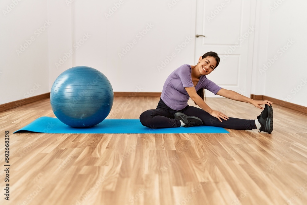 Young latin woman smiling confident stretching using fit ball at sport center Young latin woman smiling confident stretching using fit ball at sport center
