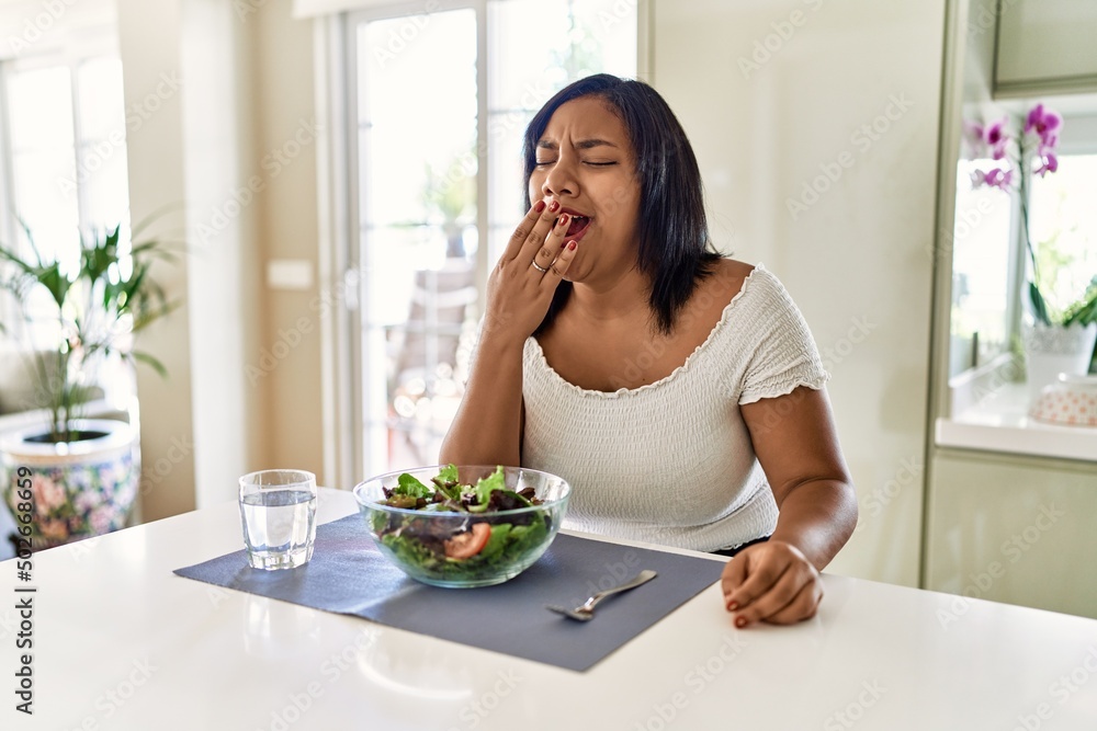 Young hispanic woman eating healthy salad at home bored yawning tired covering mouth with hand. restless and sleepiness. Young hispanic woman eating healthy salad at home bored yawning tired covering mouth with hand. restless and sleepiness.