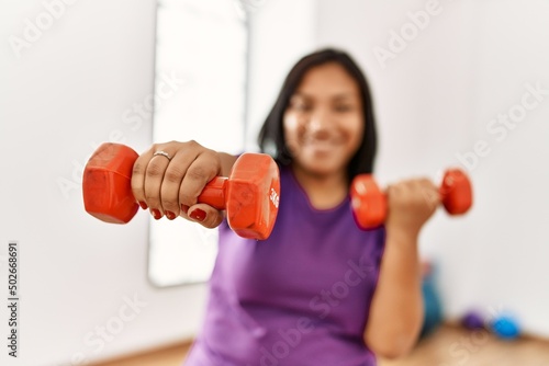 Hispanic brunette woman wearing sportwears holding weights at gym room