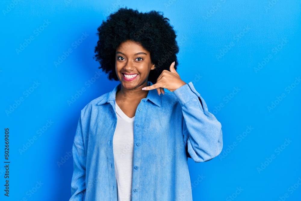 Young african american woman wearing casual clothes smiling doing phone gesture with hand and fingers like talking on the telephone. communicating concepts. Young african american woman wearing casual clothes smiling doing phone gesture with hand and fingers like talking on the telephone. communicating concepts.