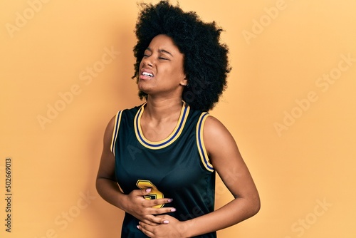 Young african american woman wearing basketball uniform with hand on stomach because nausea, painful disease feeling unwell. ache concept.