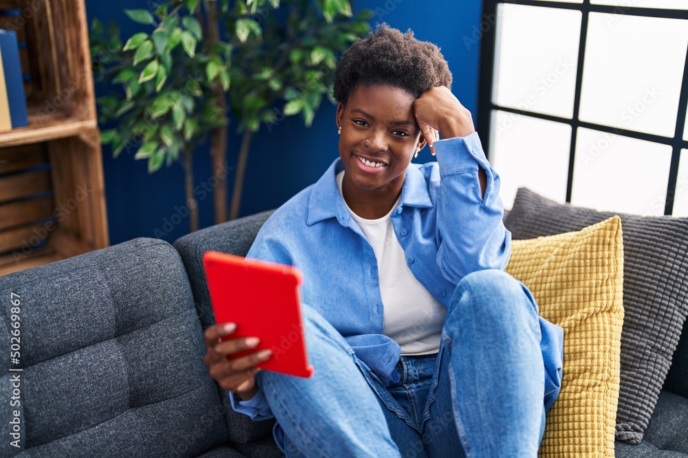 African american woman using touchpad sitting on sofa at home