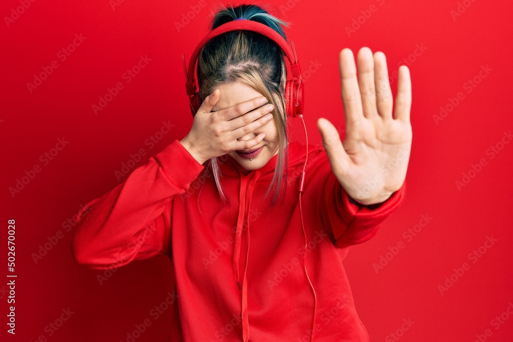 Young modern girl wearing gym clothes and using headphones covering eyes with hands and doing stop gesture with sad and fear expression. embarrassed and negative concept.