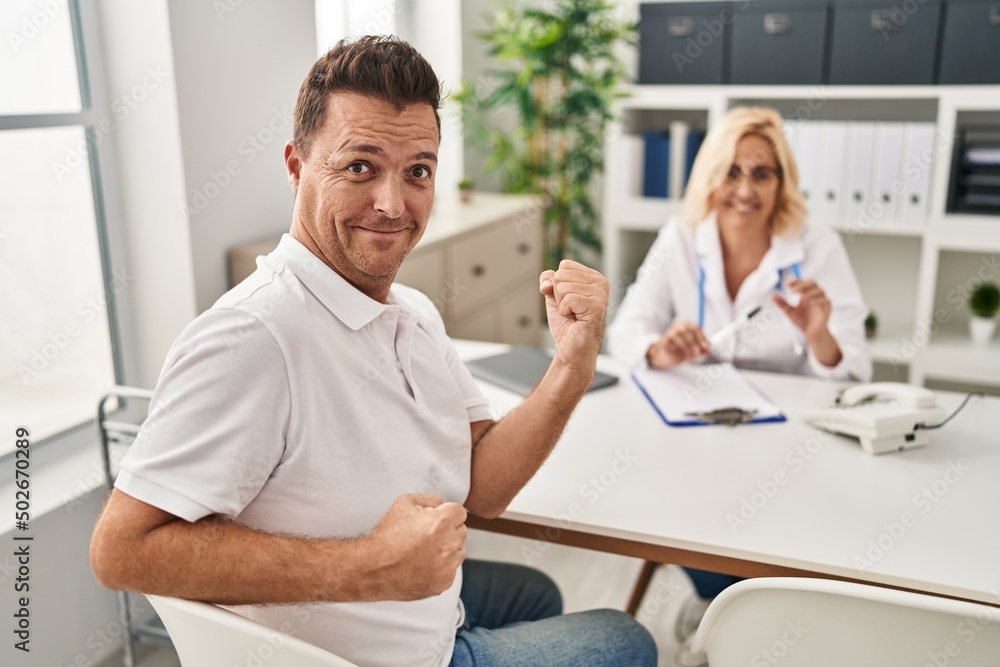 Hispanic man at the doctor screaming proud, celebrating victory and success very excited with raised arms Hispanic man at the doctor screaming proud, celebrating victory and success very excited with raised arms