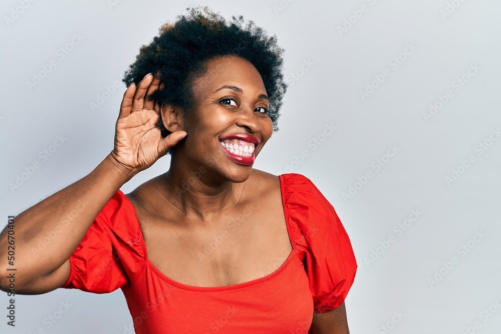 Young african american woman wearing casual clothes smiling with hand over ear listening an hearing to rumor or gossip. deafness concept. Young african american woman wearing casual clothes smiling with hand over ear listening an hearing to rumor or gossip. deafness concept.