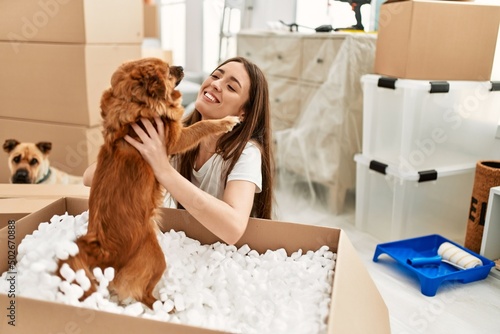 Young hispanic woman holding dog from package sitting on floor at new home