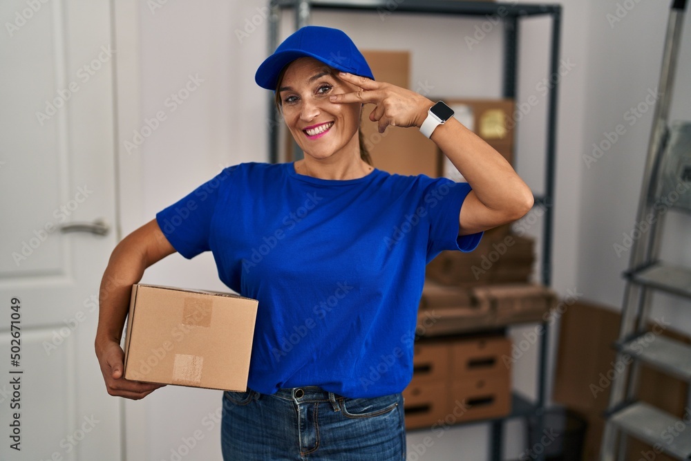 Middle age brunette woman working wearing delivery uniform and cap doing peace symbol with fingers over face, smiling cheerful showing victory Middle age brunette woman working wearing delivery uniform and cap doing peace symbol with fingers over face, smiling cheerful showing victory