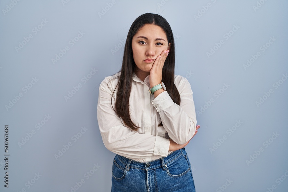 Young latin woman standing over blue background thinking looking tired and bored with depression problems with crossed arms. Young latin woman standing over blue background thinking looking tired and bored with depression problems with crossed arms.
