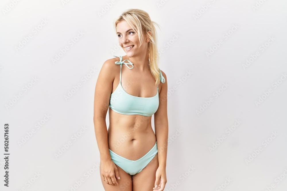 Fototapeta premium Young caucasian woman wearing bikini over isolated background looking away to side with smile on face, natural expression. laughing confident.