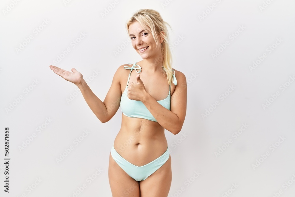 Young caucasian woman wearing bikini over isolated background showing palm hand and doing ok gesture with thumbs up, smiling happy and cheerful Young caucasian woman wearing bikini over isolated background showing palm hand and doing ok gesture with thumbs up, smiling happy and cheerful