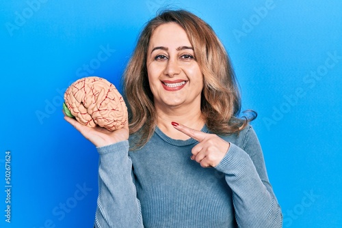 Middle age caucasian woman holding brain smiling happy pointing with hand and finger
