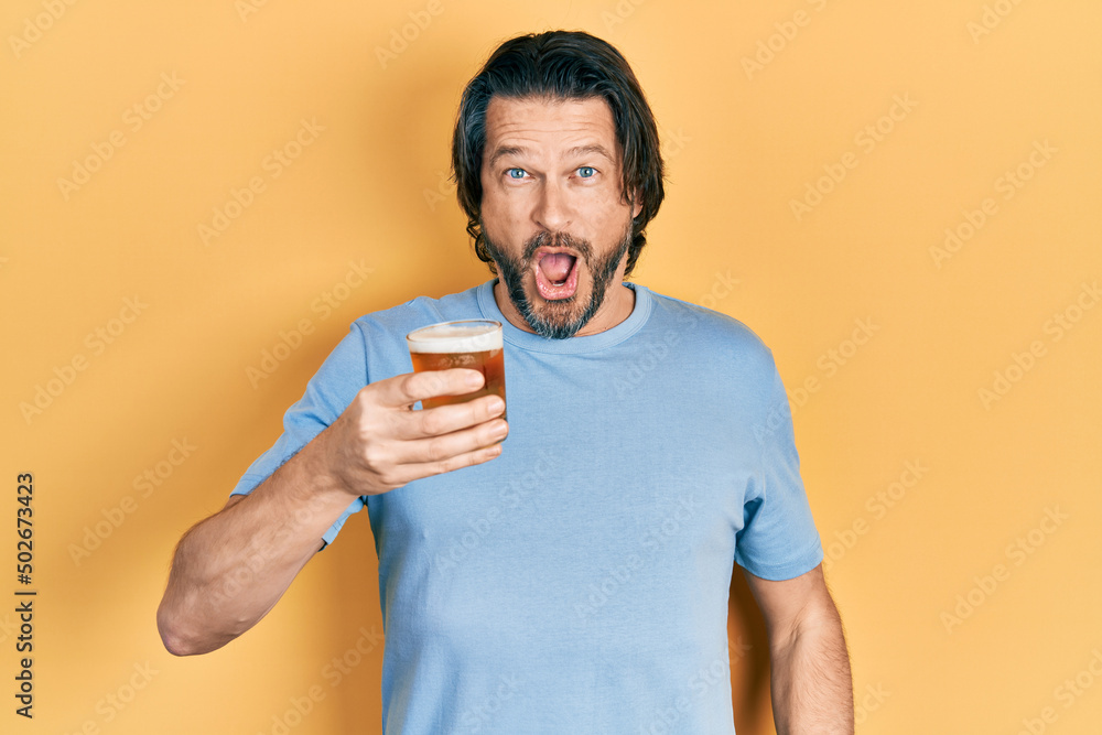 Middle age caucasian man drinking a pint of beer scared and amazed with open mouth for surprise, disbelief face Middle age caucasian man drinking a pint of beer scared and amazed with open mouth for surprise, disbelief face