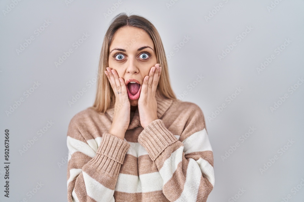 Young blonde woman wearing turtleneck sweater over isolated background afraid and shocked, surprise and amazed expression with hands on face Young blonde woman wearing turtleneck sweater over isolated background afraid and shocked, surprise and amazed expression with hands on face