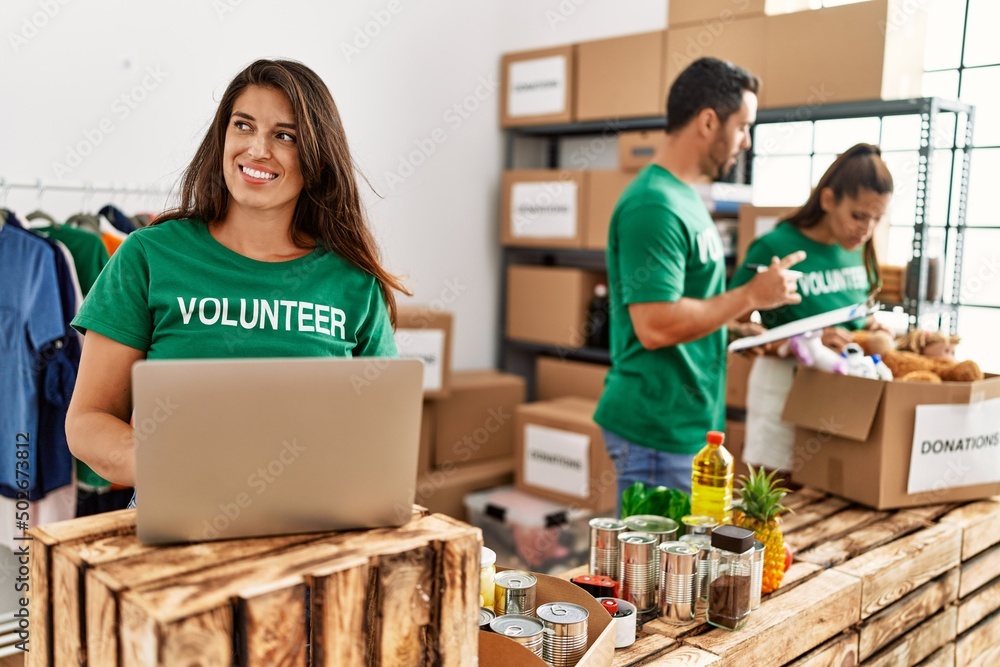 Group of hispanic volunteers working at charity center. Woman smiling happy using laptop. Group of hispanic volunteers working at charity center. Woman smiling happy using laptop.