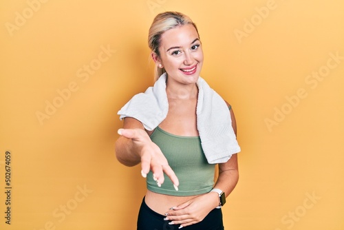Young blonde girl wearing sportswear and towel smiling cheerful offering palm hand giving assistance and acceptance. © Krakenimages.com