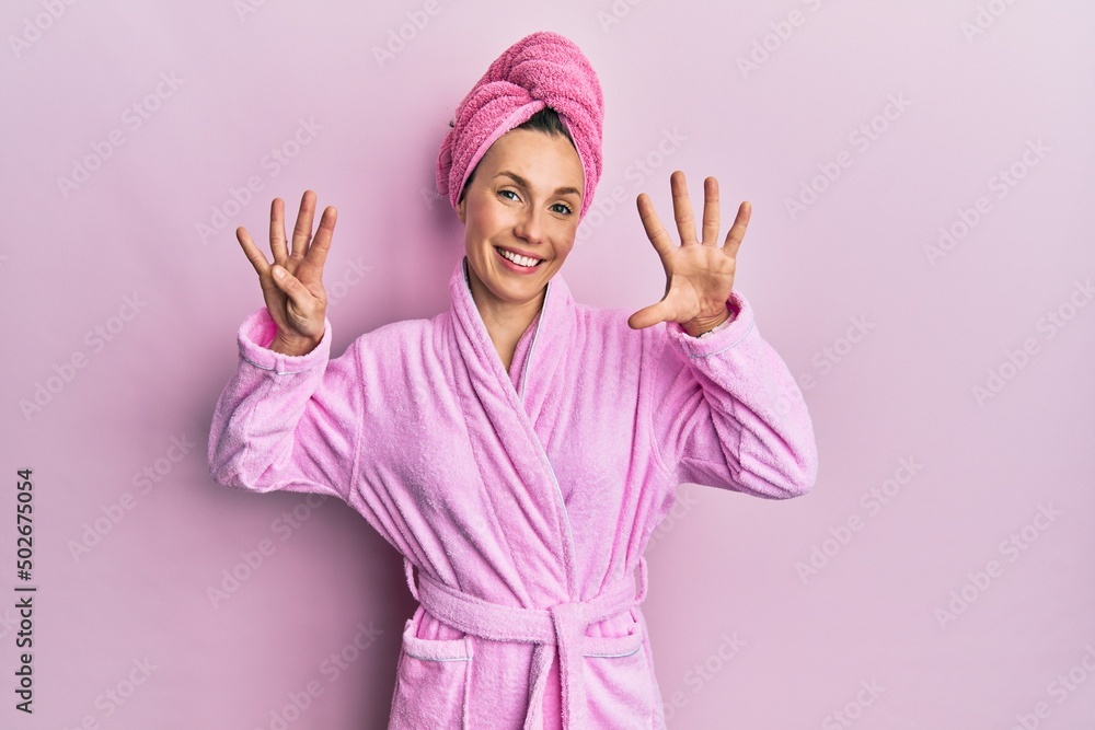 Young blonde woman wearing shower towel cap and bathrobe showing and pointing up with fingers number nine while smiling confident and happy. Young blonde woman wearing shower towel cap and bathrobe showing and pointing up with fingers number nine while smiling confident and happy.