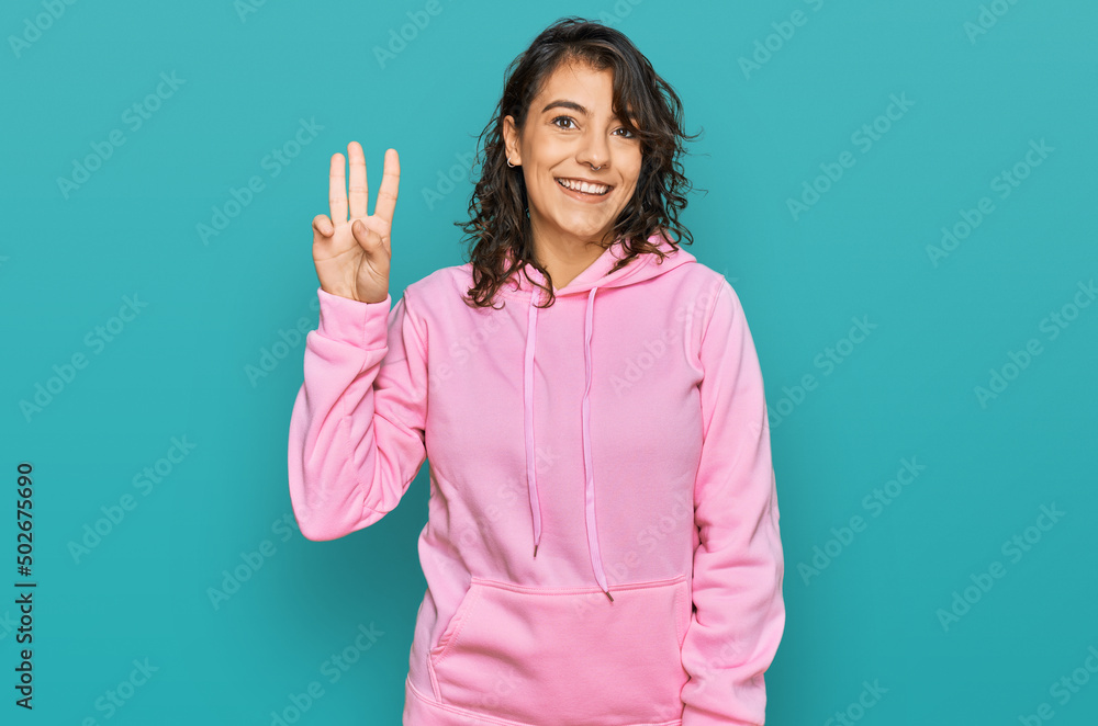 Young hispanic woman wearing casual sweatshirt showing and pointing up with fingers number three while smiling confident and happy. Young hispanic woman wearing casual sweatshirt showing and pointing up with fingers number three while smiling confident and happy.