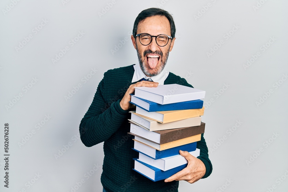 Middle age hispanic man holding a pile of books sticking tongue out happy with funny expression. Middle age hispanic man holding a pile of books sticking tongue out happy with funny expression.
