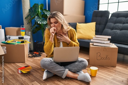 Young woman sitting on the floor at new home using laptop feeling unwell and coughing as symptom for cold or bronchitis. health care concept.