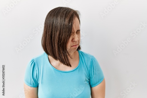 Young down syndrome woman standing over isolated background with hand on stomach because nausea, painful disease feeling unwell. ache concept.